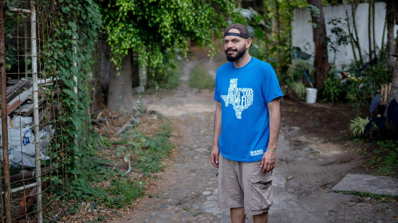 Carlos Cordero in a hat and blue shirt stands in a leafy laneway.