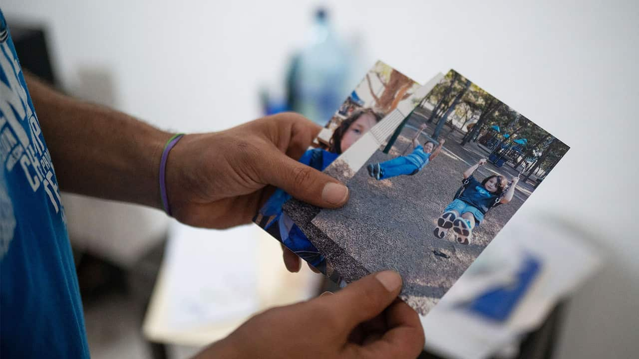 A man holds pictures of a child and his mother on a swing