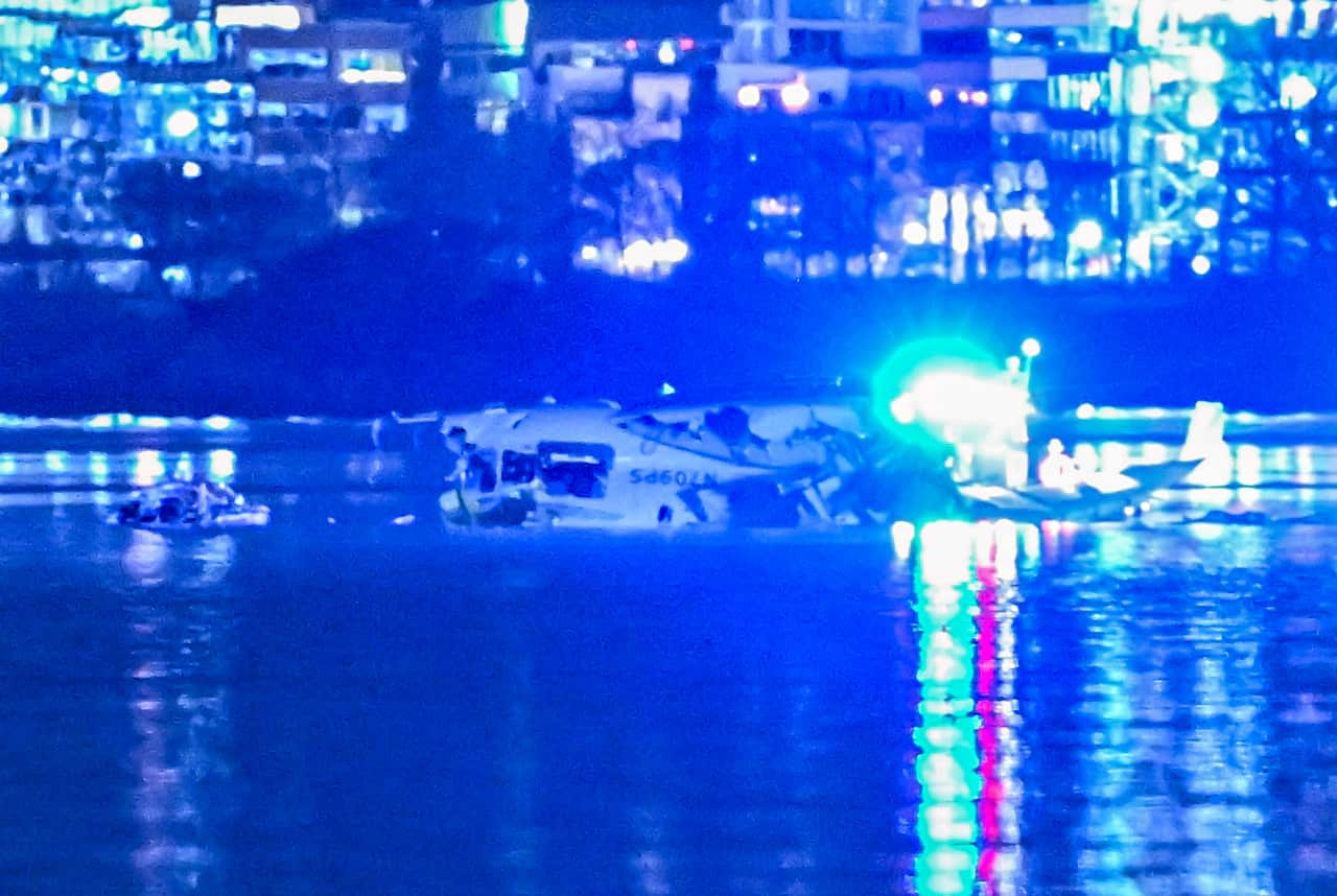 Wreckage of a plane in a river as blue lights reflect in the water.