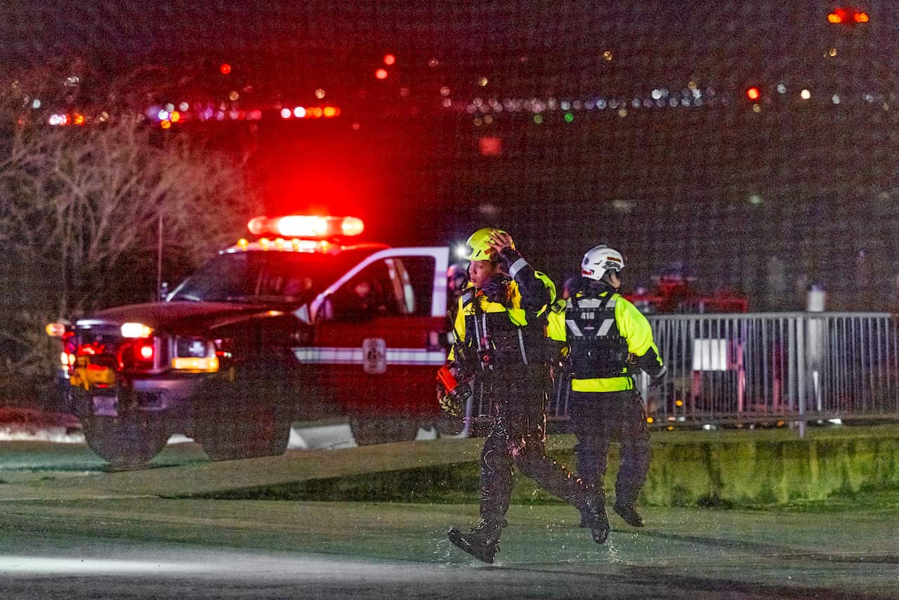 Two rescue workers walk in opposite directions with a police vehicle parked nearby.