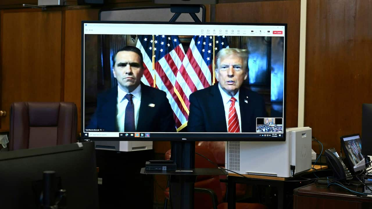 Donald Trump and a man in a black suit appear on a TV screen inside a courtroom.