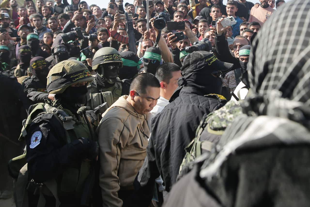 Masked men in military attire escort men amidst a big crowd