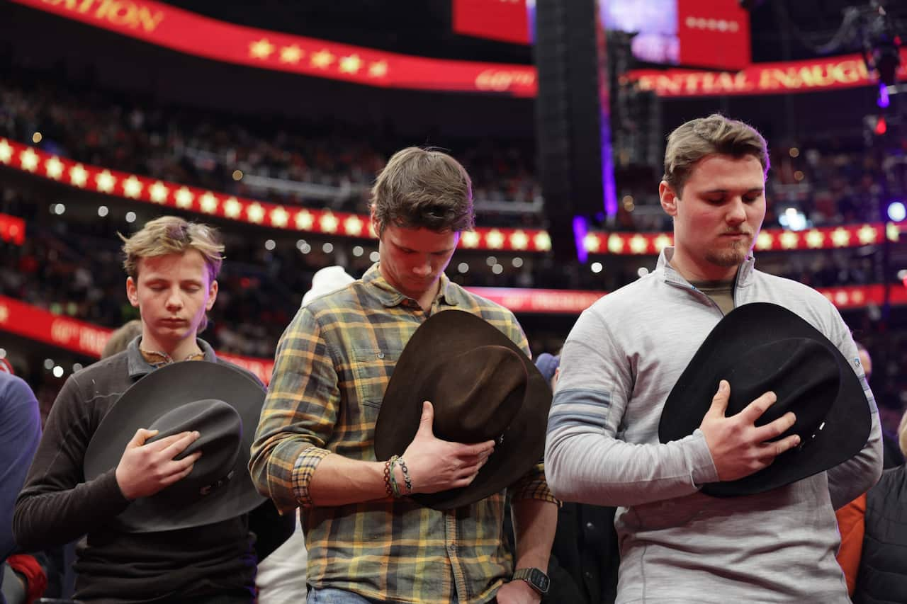 Men bowing heads, clutching hats to chest.