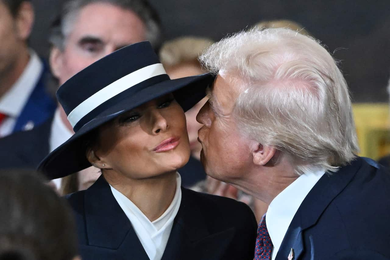 Donald Trump gives his wife, Melania Trump, a kiss on the cheek, who is wearing a wide-brimmed hat.