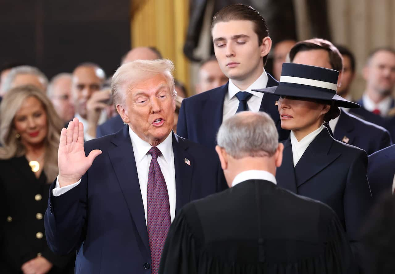 Donald Trump, with his hand raised, swears the oath of office. He is surrounded by a group of people.