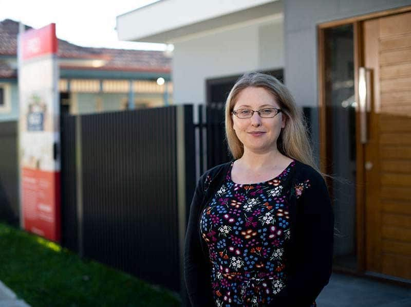 headshot of a woman with a flowery top and a fence behind her