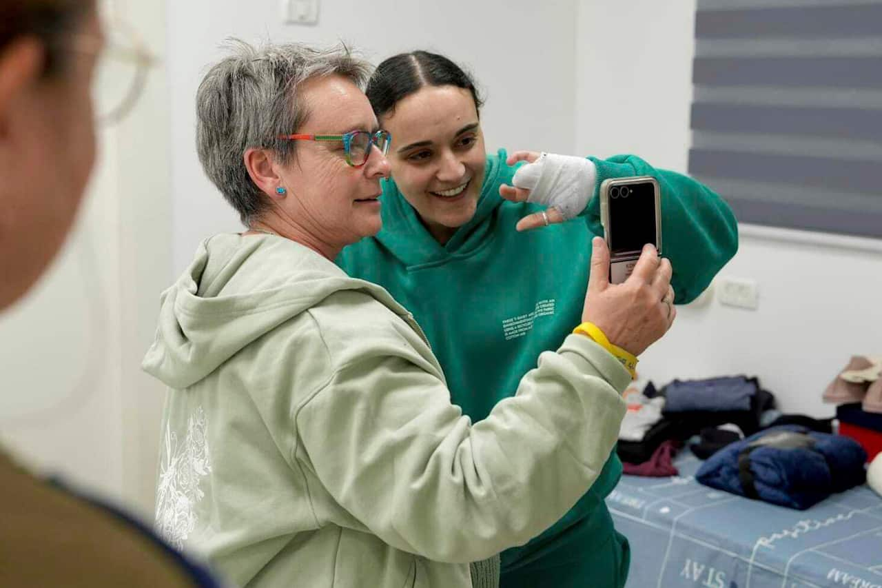 An elderly woman holds a phone while standing next to a young woman, both looking at the screen.