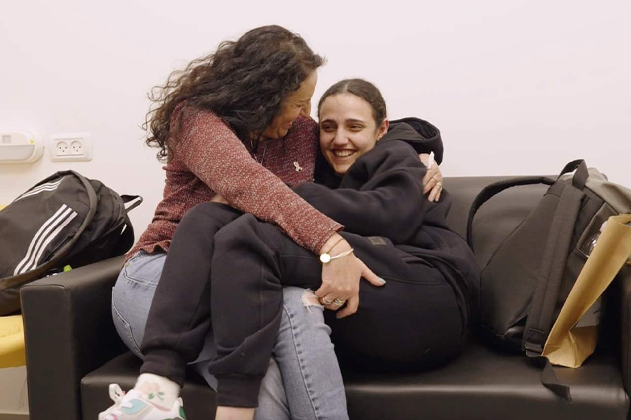 A woman in a black tracksuit is sitting in another woman's lap.