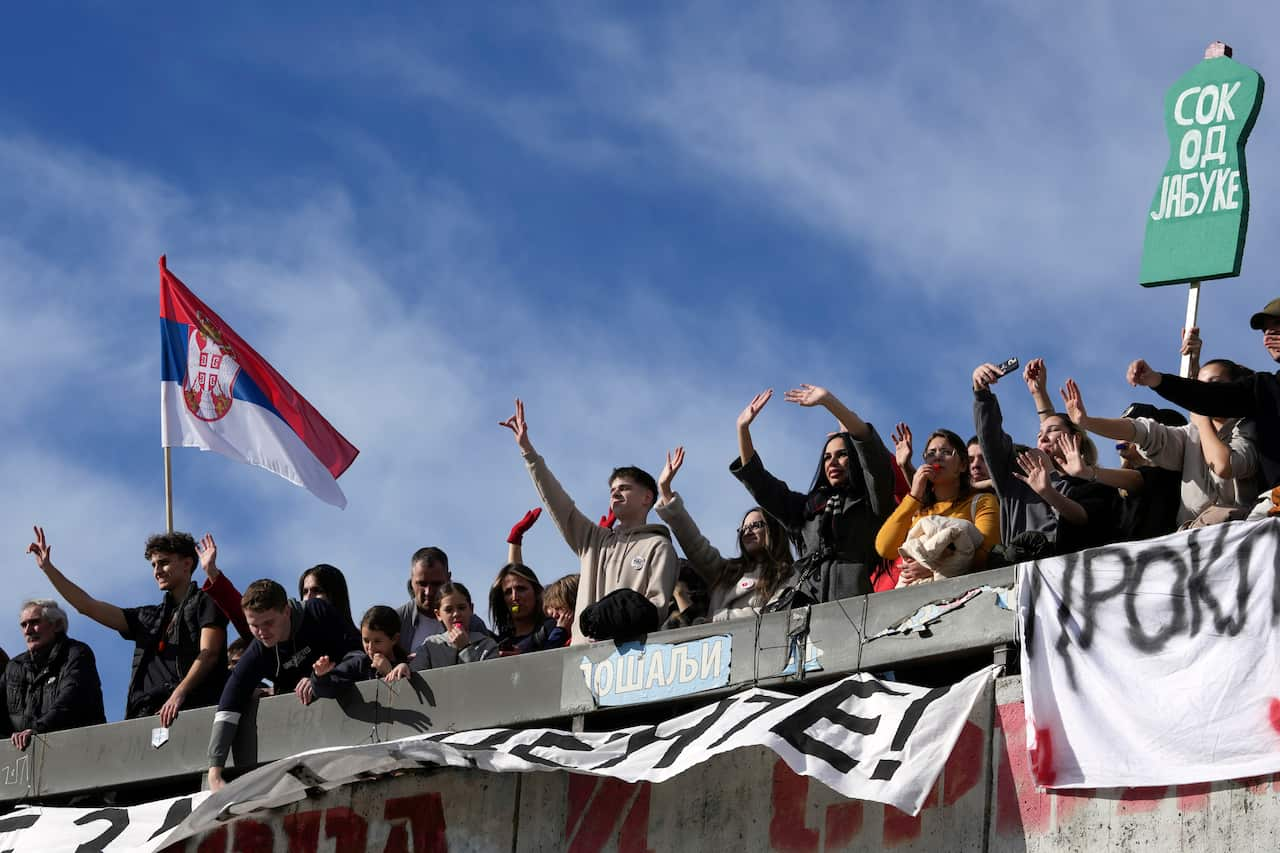 A large group of protesters standing on a bridge and chanting.