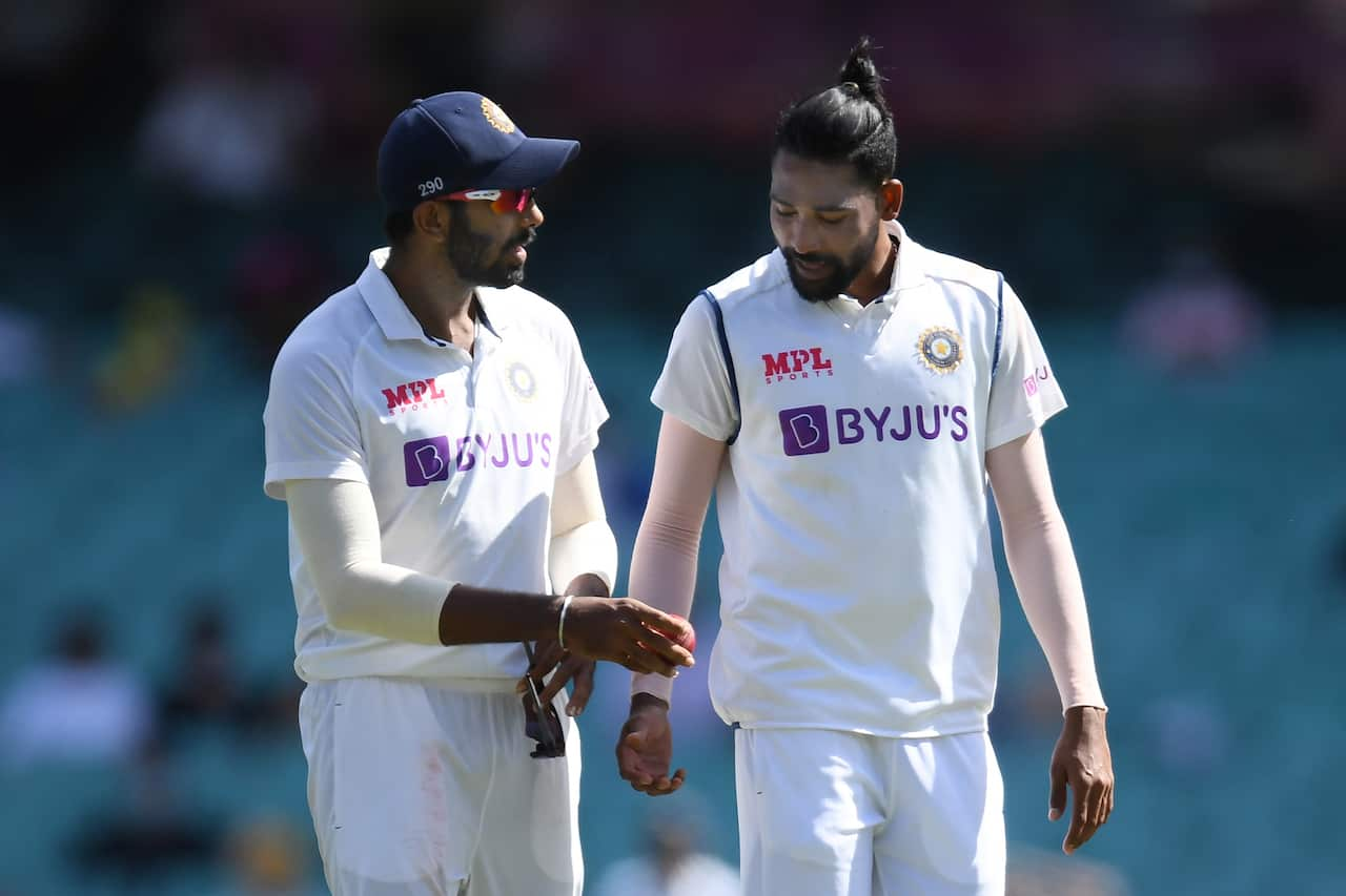 Two cricket players in white test match clothing are talking on the field.