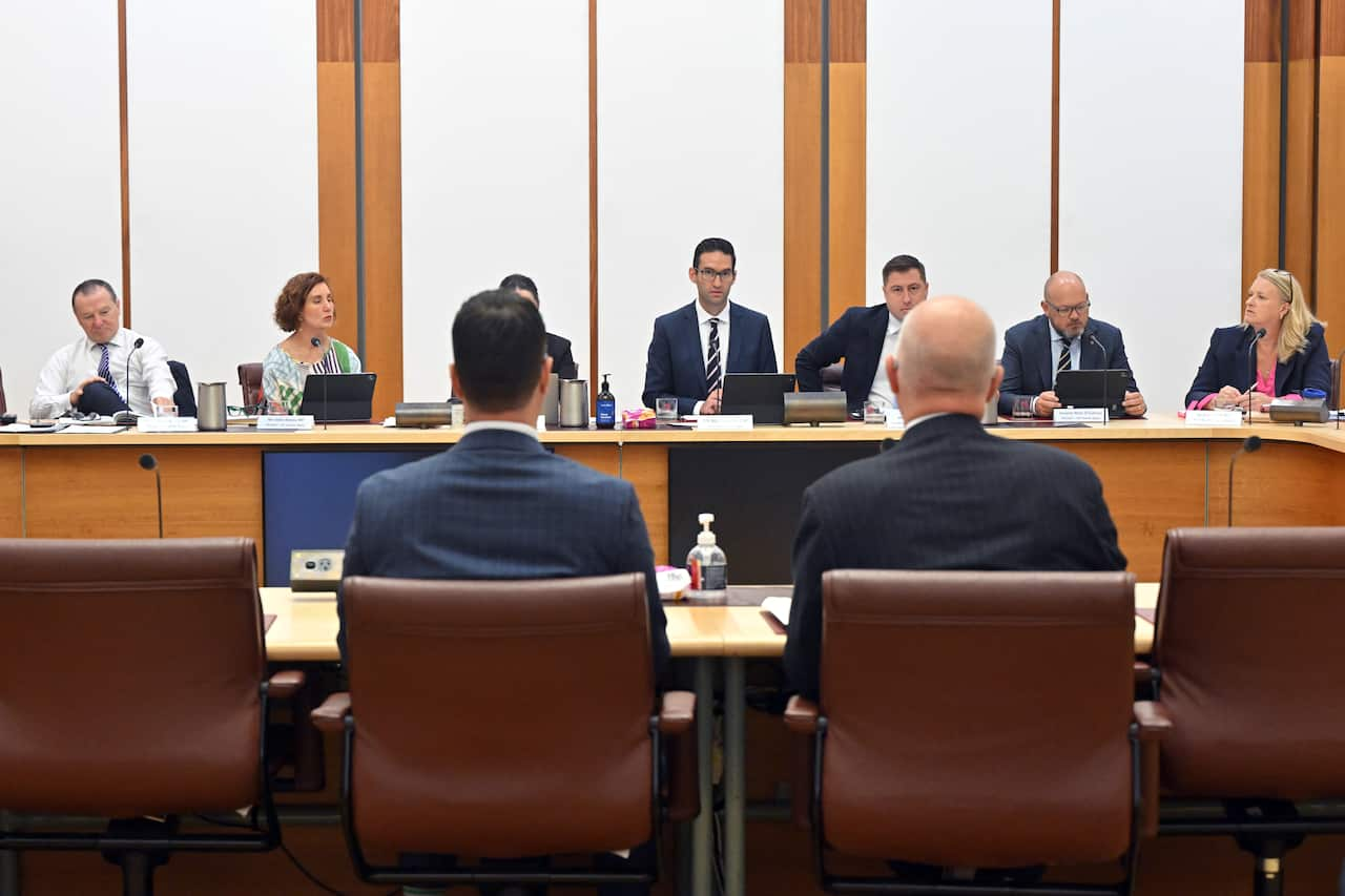 Men and women sitting across each other in a committee room.