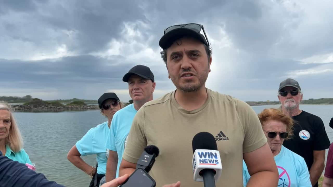 A man in a t-shirt speaking to journalists.