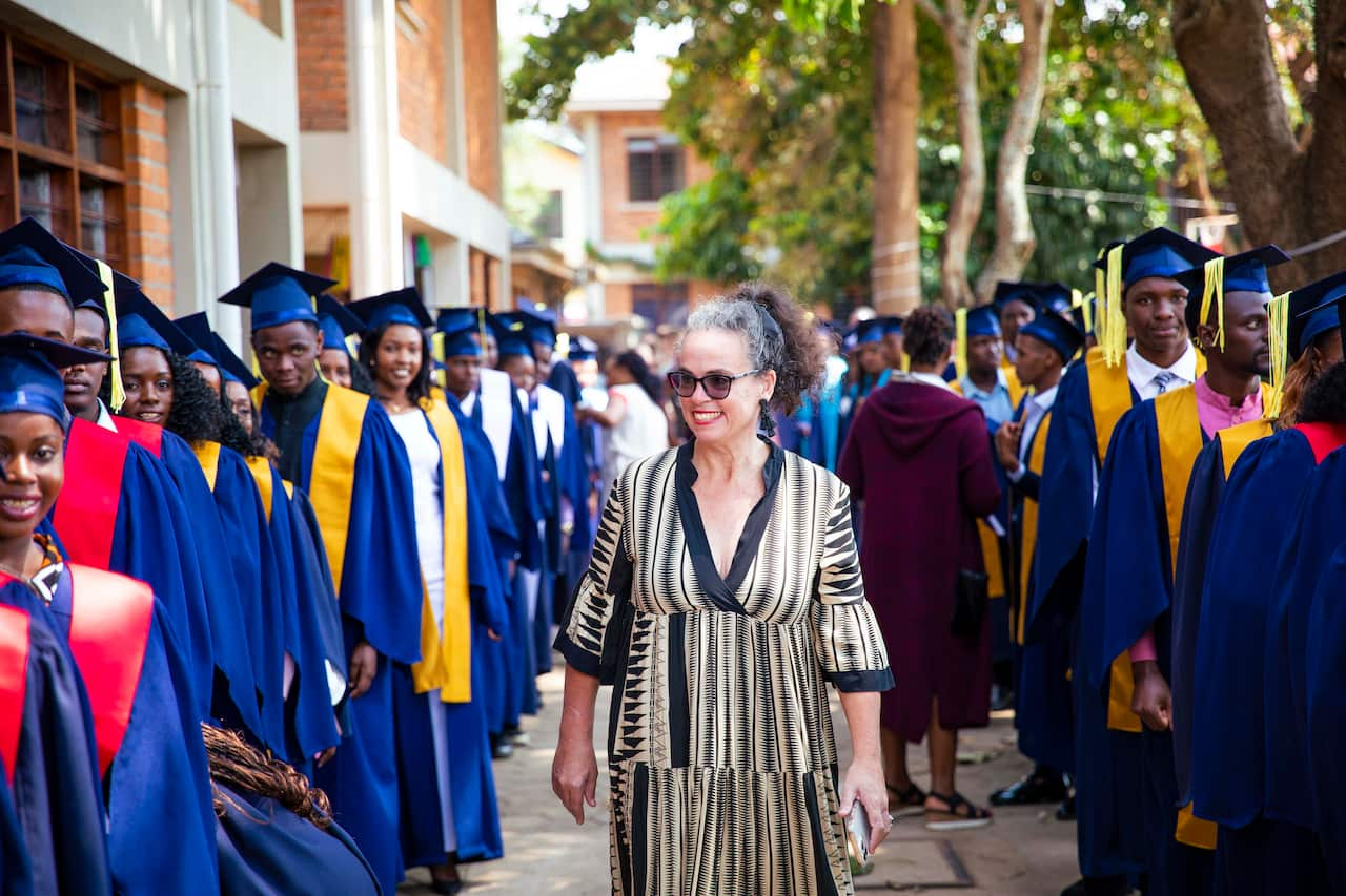 A woman smiles as she walks among a group of university graduates wearing blue robes and mortar-board hats