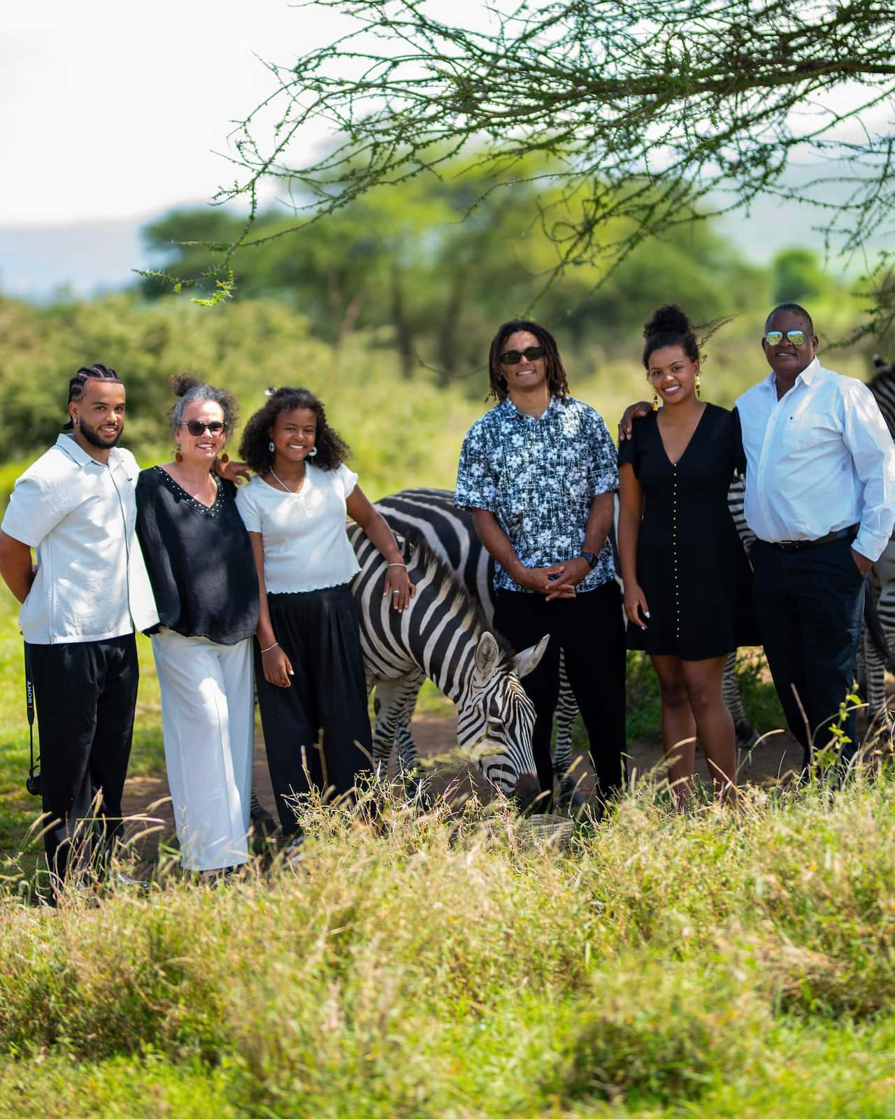 A family – plus a zebra – stand among trees and smile.