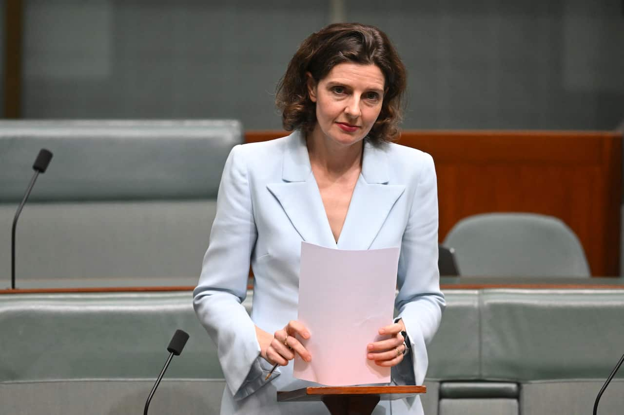 A woman in a light blue jacket, holds pieces of paper in front of her.