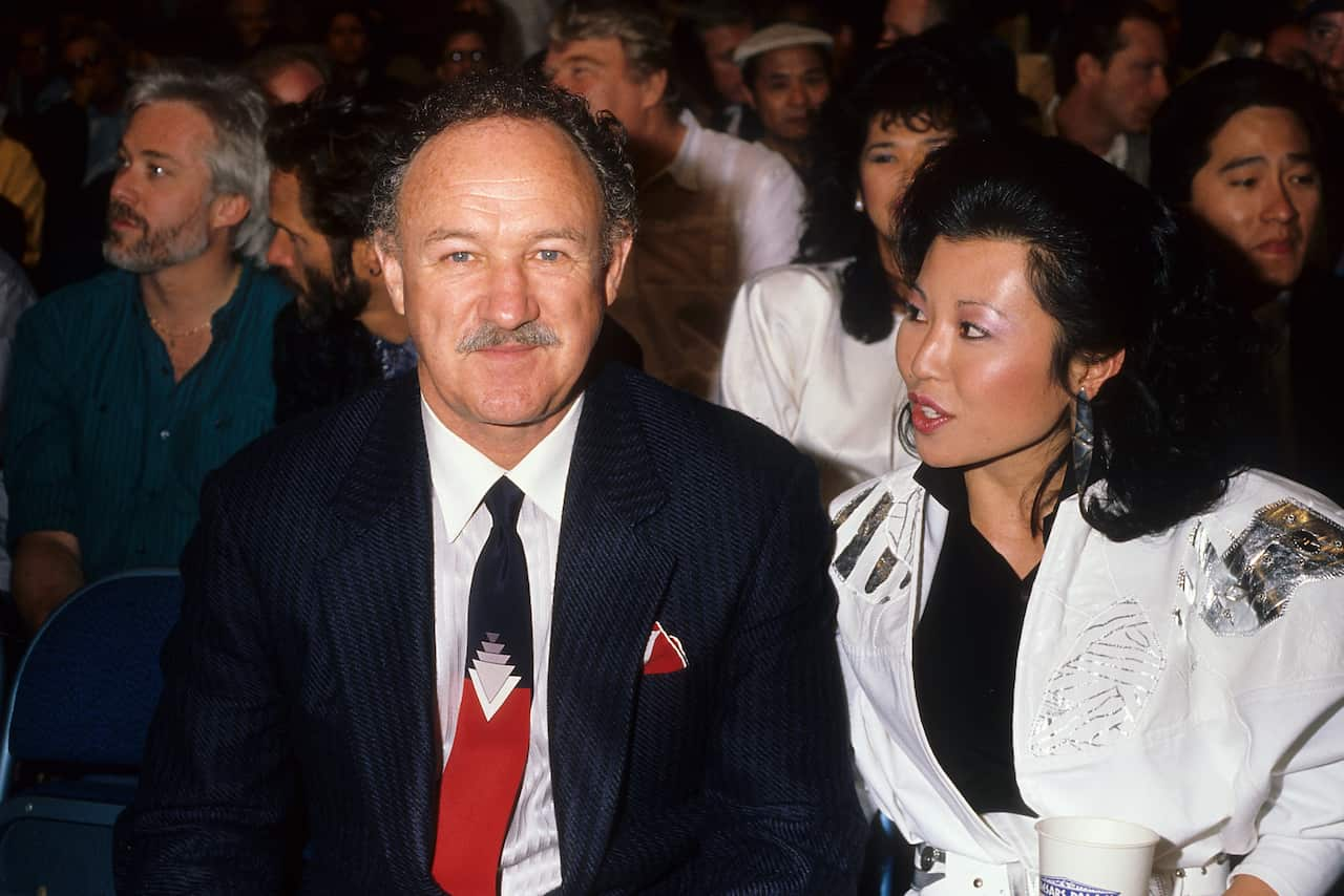 A man in a black suit (left) is sitting next to a woman in a white dress in an audience.