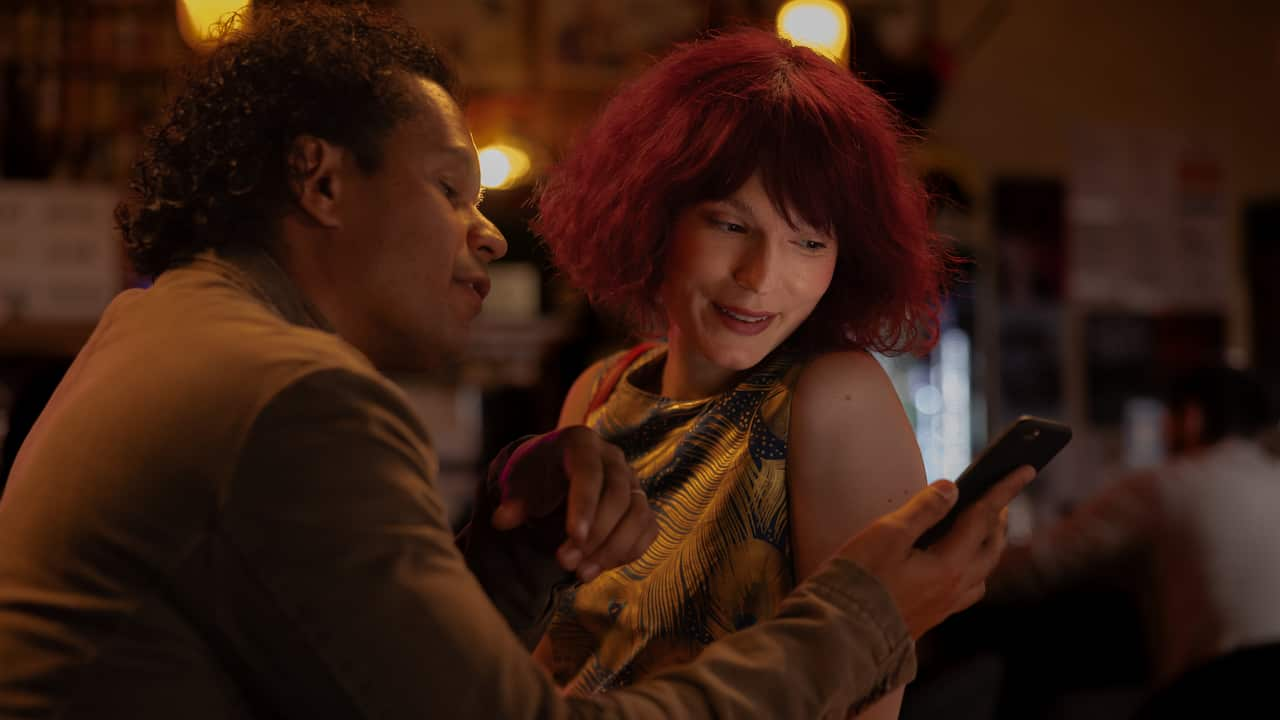 A man and a woman looking at a phone in a bar.