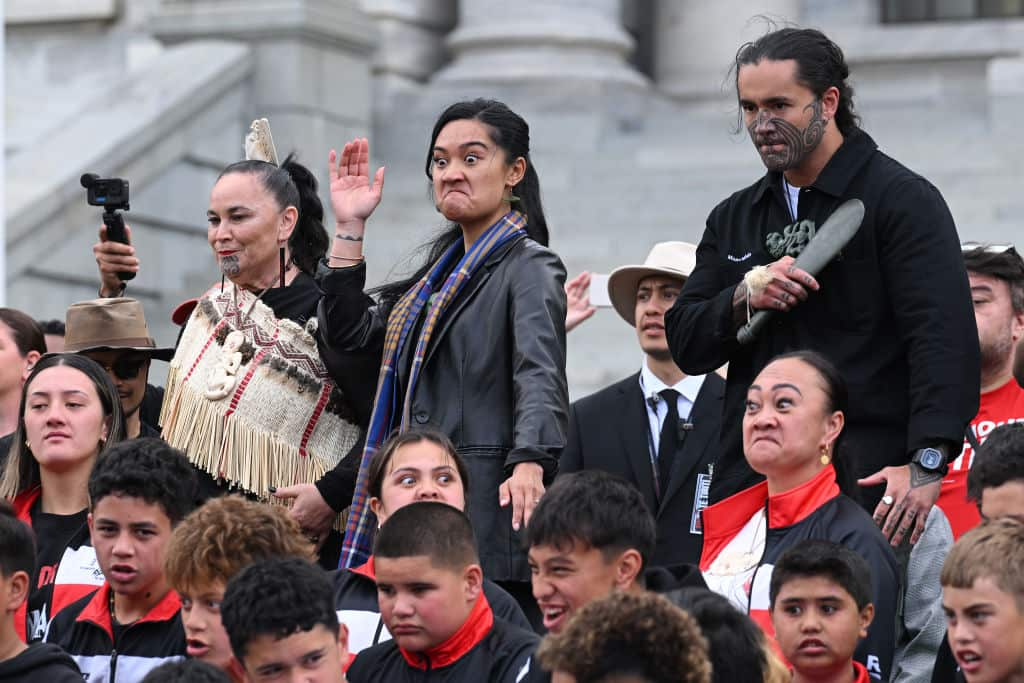 Two Māori women and a man performing haka during a protest.