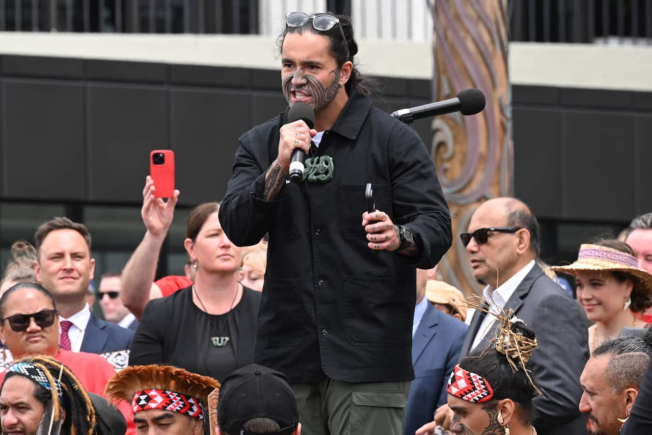 A man with face tattoos is speaking into a microphone during a rally.