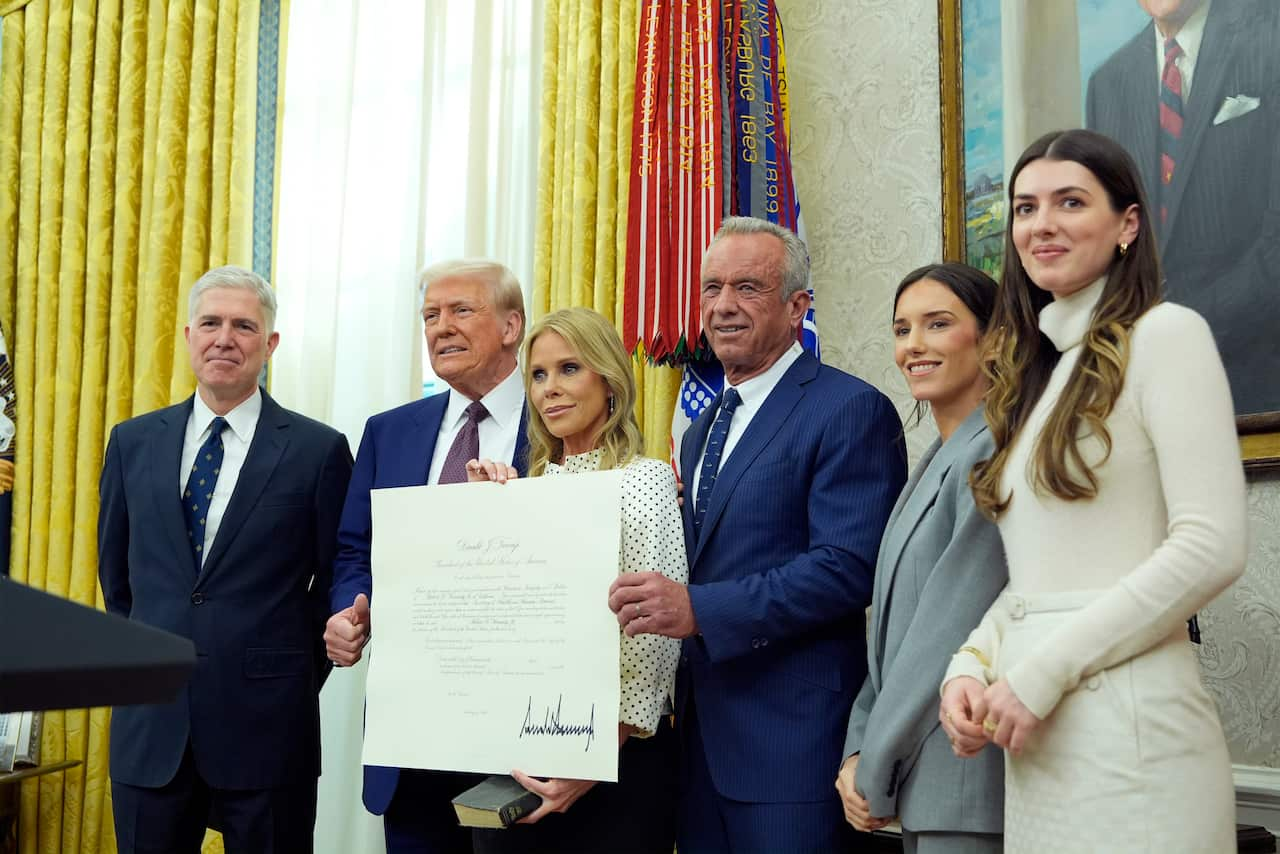 A group of people in formal attire pose for a picture with a woman in the centre holding a large order.